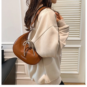 Close-up of brown leather crescent bag with white pearl bow charm and fashion print