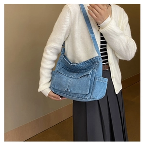 Detail shot of a blue denim crossbody bag featuring utility flap pockets and soft wash texture