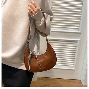 Close-up of brown crescent underarm bag with glossy patent leather and beaded bow detail