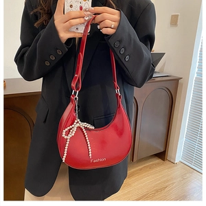 Close-up of red glossy crescent shoulder bag with pearl bow and Fashion lettering