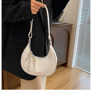Detailed shot of a white crescent shoulder bag featuring a pearl bow charm and PU leather