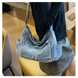 Close-up of blue denim crossbody bag featuring utility pockets and adjustable strap on a model
