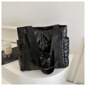 Detailed close-up of glossy black quilted down tote bag on minimalist white display stand