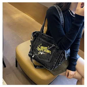 Detail of black denim tote bag with yellow embroidery and pearl chain strap on model