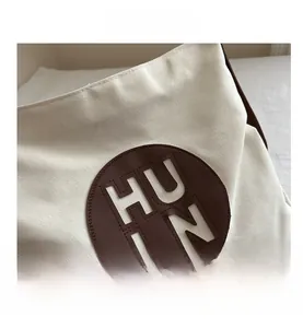 Detailed close-up of canvas tote bag with brown leather H-logo patch and texture