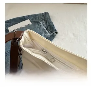 Detail view of the smooth silver zipper closure and brown leather strap on canvas tote bag