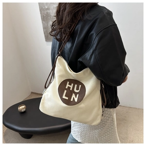 Detail of a minimalist canvas tote bag with brown leather patch and shoulder strap detail