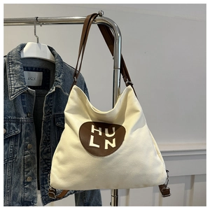 Detail of canvas hobo bag with brown leather patch and logo on metal hanger backdrop