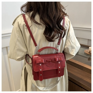 Red British style backpack with heart stitching and bows worn over a trench coat