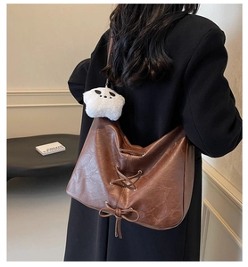 Detail of dark brown faux leather tote bag with lace-up decor and panda plush charm