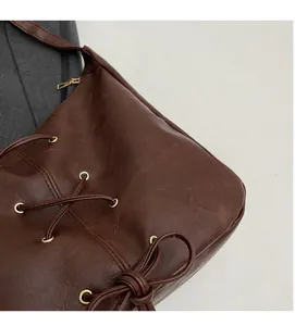 Detail of brown faux leather bag with lace-up bow design and gold metal eyelets