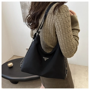 Detail of black nylon shoulder bag featuring a metal triangle logo and chain strap