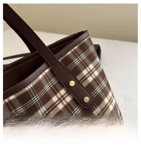 Close-up of brown plaid canvas tote with premium leather straps and gold metal rivets