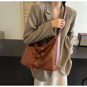Détail d'un sac hobo en cuir marron avec des accents décoratifs de lacets et de nœuds