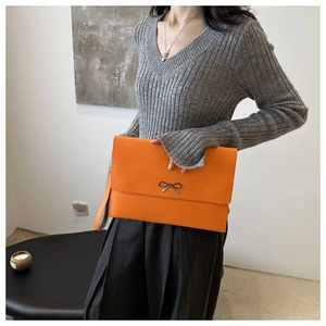 Slim orange envelope clutch bag featuring a metallic bow detail and wristlet strap