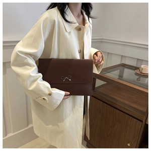 Detailed view of large dark brown envelope clutch bag with silver bow accent in daily use