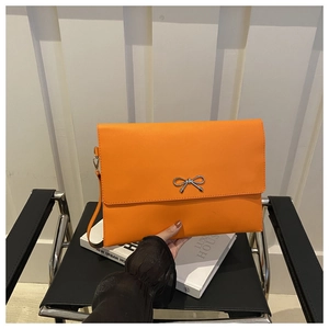 Detailaufnahme der leuchtend orangefarbenen Briefumschlagtasche mit silberner Schleife