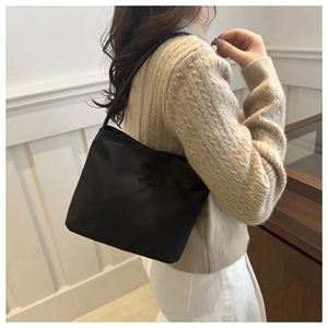 Detail of black nylon tote bag with embossed text on model in minimalist interior