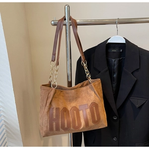 Detail of brown suede tote bag with HOOTO letter patch and gold chain strap handle