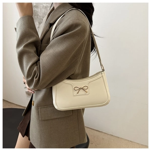 Detail of a chic cream-white shoulder bag with a gold bow metal buckle on a khaki blazer
