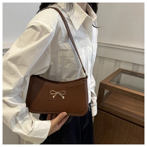 Detail of brown leather baguette bag with elegant golden bow buckle worn on shoulder
