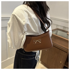 Detail shot of brown shoulder bag with golden bow hardware and faux leather texture