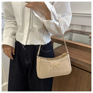 Detail of beige shoulder bag with golden bow ornament and smooth faux leather texture