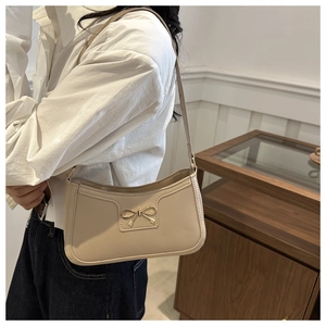 Detail of beige baguette bag featuring a gold metal bow and shiny leather texture