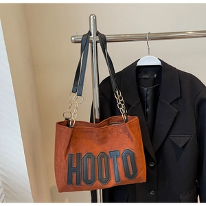 Detail of brown suede tote bag with HOOTO letter print and gold chain strap attachment
