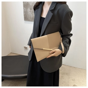 Beige envelope clutch bag with gold metal buckle detail shown in casual urban setting