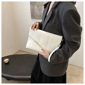 Close-up of white patent leather clutch bag with gold metal trim and flap design