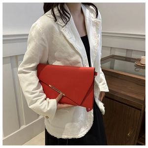 Detail of a red envelope clutch bag featuring an irregular flap and gold metal hardware