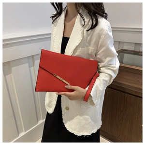 Chic red leather envelope clutch with gold metal bar held by model in white blazer