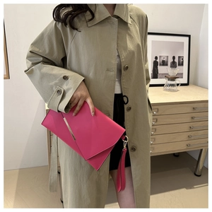 Magenta envelope clutch bag with gold trim and long tassel detail styled with a trench coat