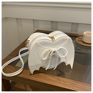 Sac à main blanc en forme de cœur avec ailes de chauve-souris et nœud sur table