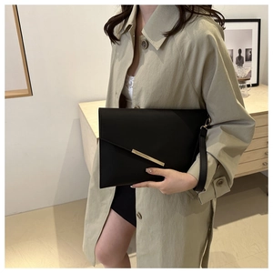 Detail of black envelope clutch bag with gold metal trim and detachable wrist strap
