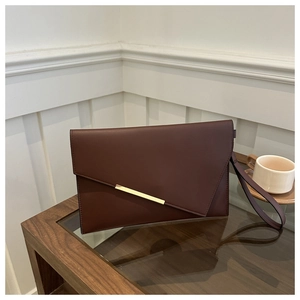 Close-up of burgundy envelope clutch bag with gold metal buckle on a glass table
