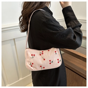 Pink corduroy shoulder bag with cherry print worn by a model against a clean wall