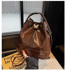 Detail of dark brown glossy patent leather bucket bag with silver butterfly drawstring clasp