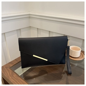 Detail of black envelope clutch bag featuring sleek matte texture and gold metal accent