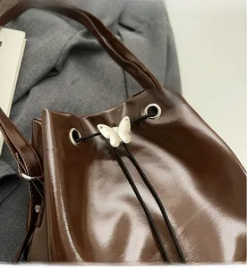 Detail of dark brown glossy leather bucket bag featuring a silver metal butterfly clasp