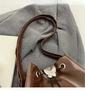 Detail of dark brown glossy bucket bag featuring silver butterfly buckle and thin strap