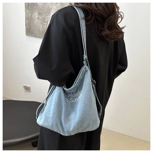 Rear view of a model wearing a light blue denim tote bag with minimalist white text