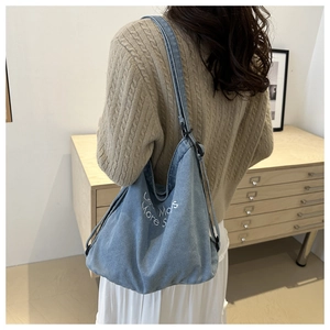 Detail of light blue denim tote bag with Less More embroidery and adjustable strap