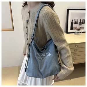 Detail of light blue denim hobo bag with Less Mondays More Sundays white embroidery text