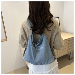 Detail view of light blue denim tote bag with drawstring closure and text on beige knitwear