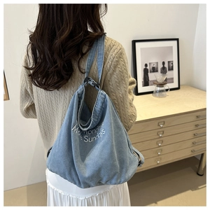 Detail of embroidered lettering on a light blue washed denim tote bag for women