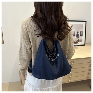 Detail of dark blue denim tote with white embroidered text on a casual shoulder bag