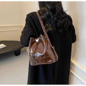 Close-up of brown patent leather bucket bag with silver butterfly charm and drawstring