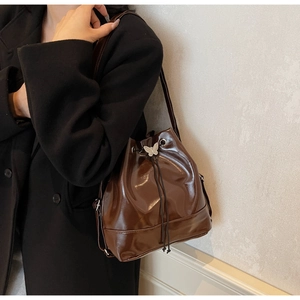 Detail of a dark brown glossy bucket bag with drawstring closure and silver butterfly charm